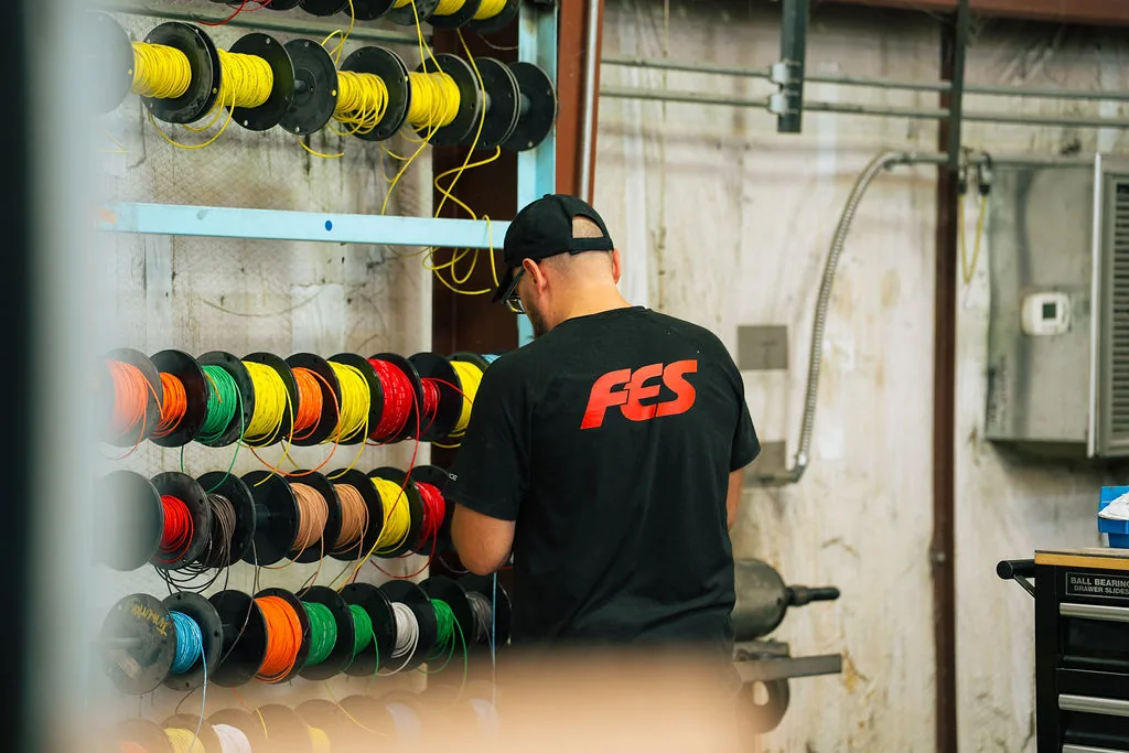 FES team member in a shop shirt selecting wire from the color coded harness rack