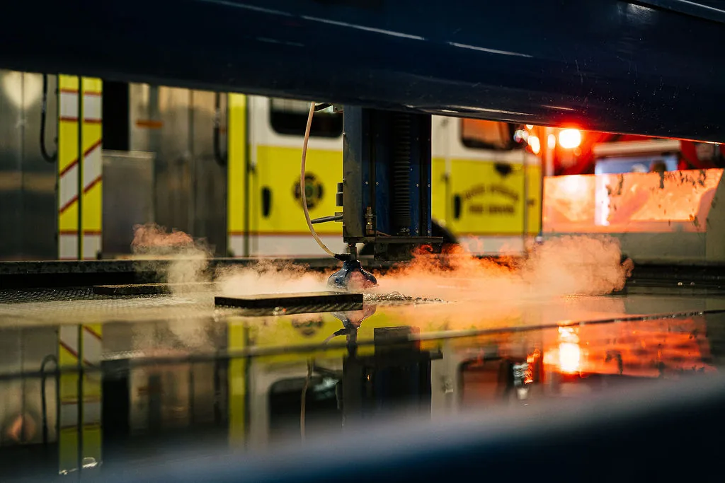 CNC cutting table running a part with a fire apparatus reflected on the FES shop floor