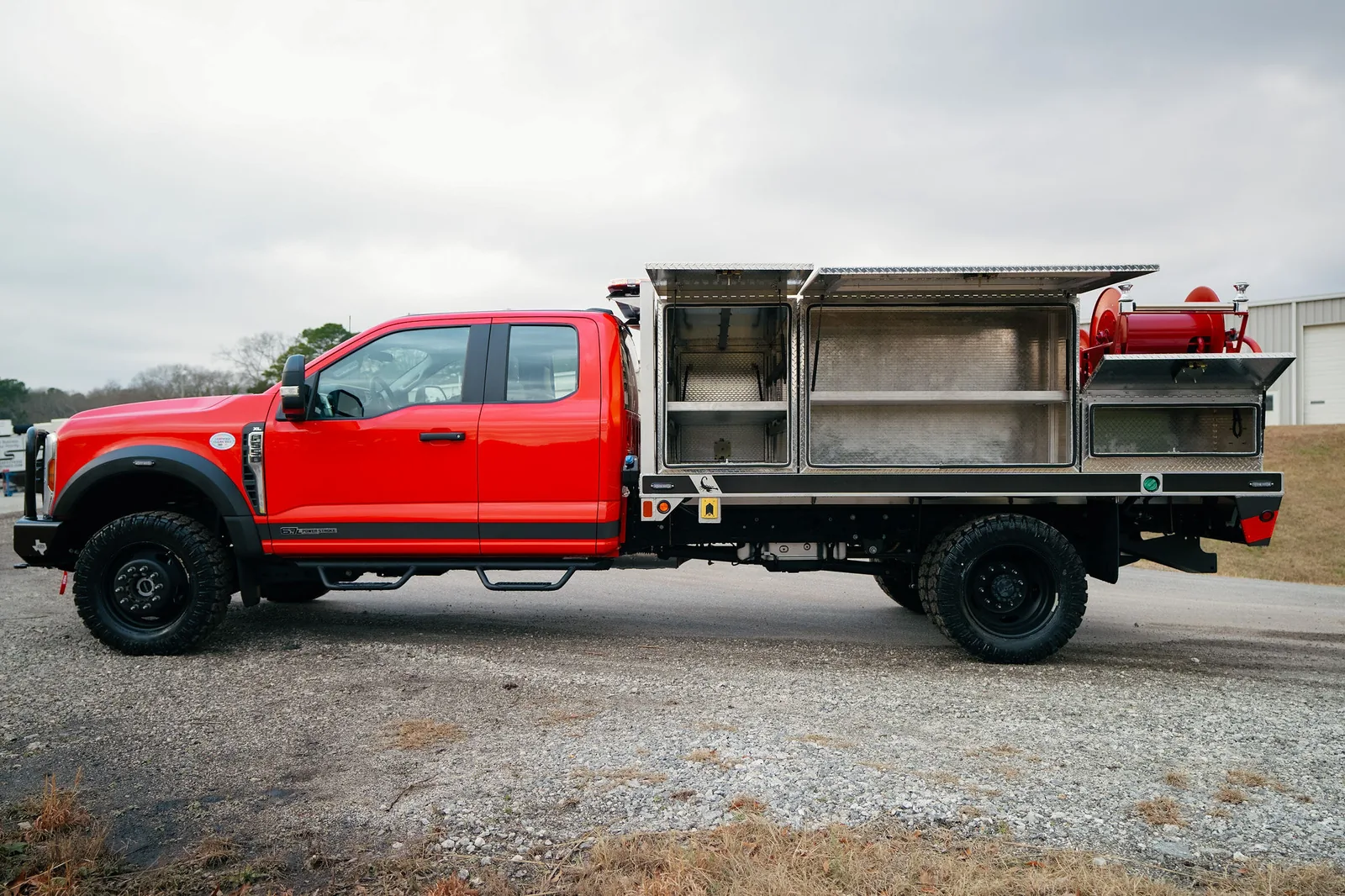Red FES brush truck with flatbed aluminum body, open compartments, and hose reels